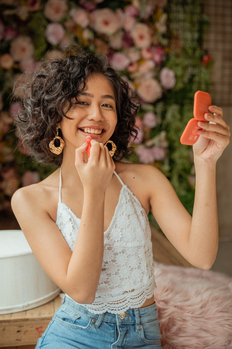 Smiling Woman Applying Lip Gloss and Holding a Compact Mirror